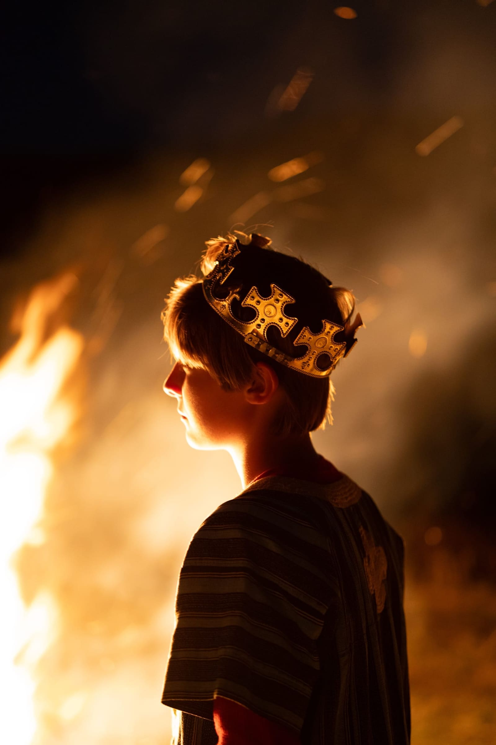 Boy in a gold crown rim-lit by falling sparks